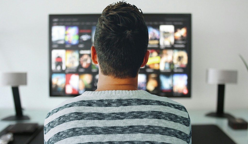une personne assise devant la télévision et regarde un écran, il profite de son cadeau pour un homme qui aime les voyages, un abonnement pour une chaîne TV de voyage