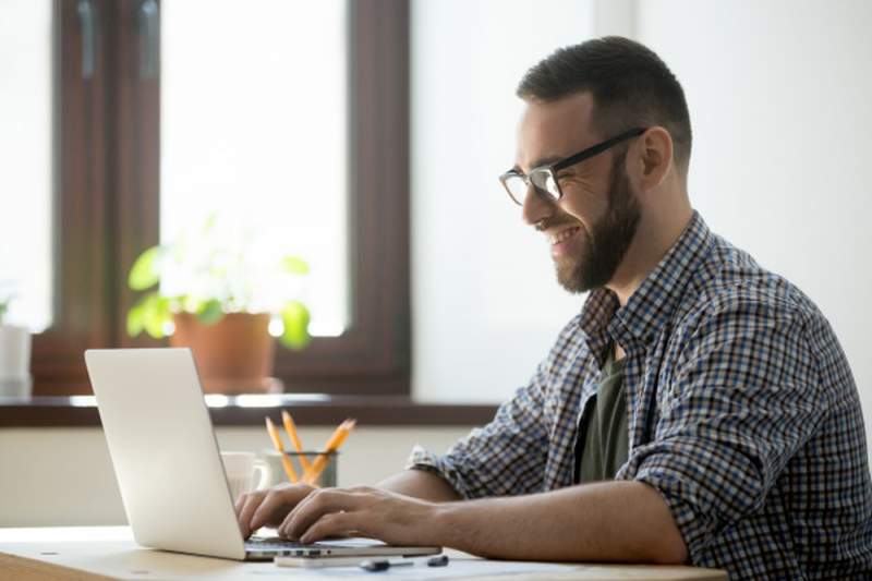 un homme assis à un bureau devant son pc portable assite à des cours de langue en ligne qu'il lui ont été offert avant son prochain tour du monde