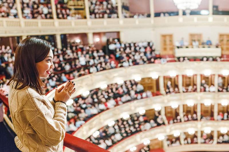 une jeune femme applaudit debout une représentation au niveau du balcon dans une salle de théâtre, lors d'une de ses activités à faire à paris à un spectacle,