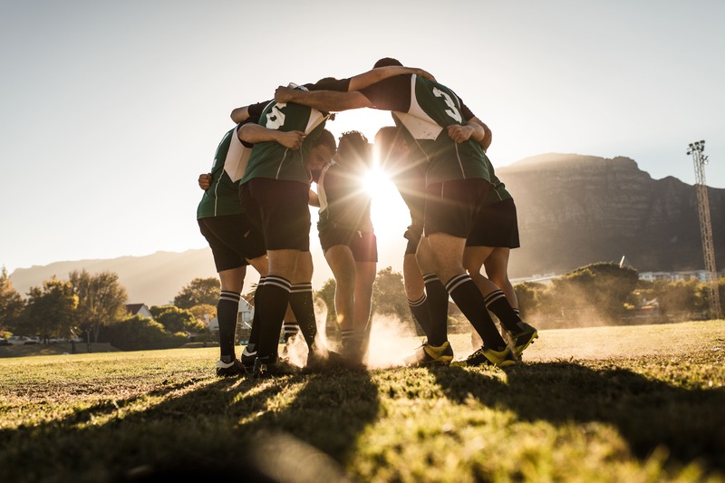 un homme qui aime le rugby s'entraine avec ses coéquipiers sur une pelouse verte. Ils se tiennent en cercle.