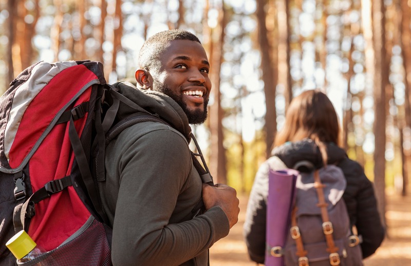 un homme souriant qui aime voyager est dans la nature en forêt avec un sac à dos