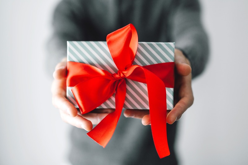 un homme tient en main un cadeau emballé qu'il offre à un homme