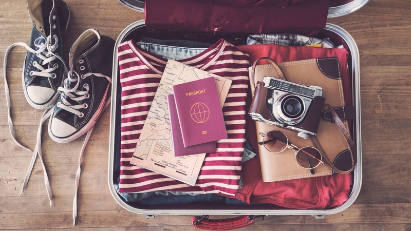 une valise de vacances préparée pour ne rien oublier : passeport, plan de ville, lunette de soleil, chapeau