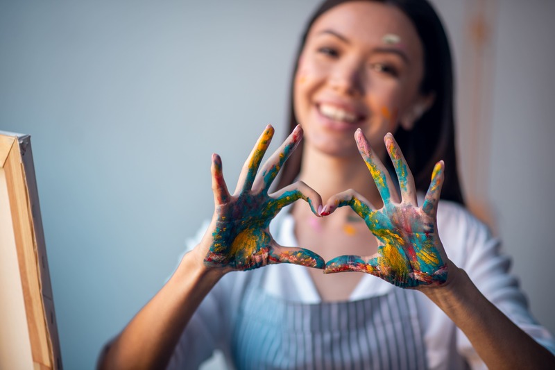 Femme souriante qui peint et fait le symbole de l'amour, un coeur avec ses mains